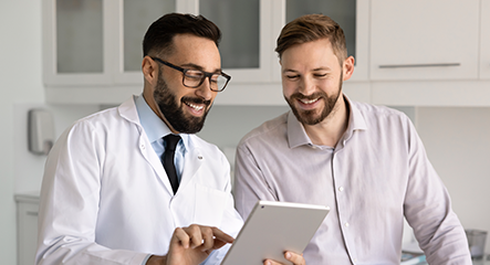 Médico e paciente sorrindo enquanto visualizam informações em tablet digital.