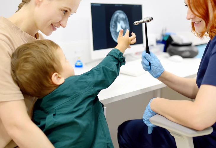 Criança sentada no colo da mãe em frente a médica