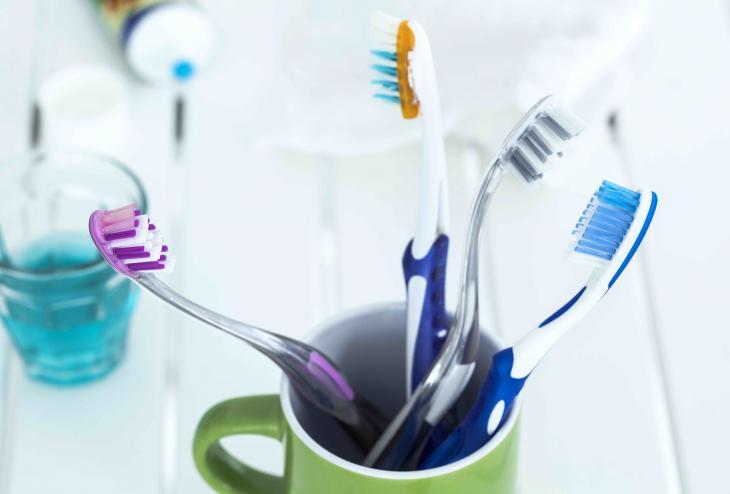Imagem de uma caneca com 4 escovas de dentes dentro, e ao fundo uma pasta de dente sem a tampa