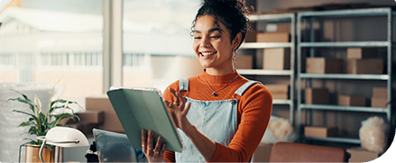 Mulher usa tablet sorrindo em ambiente de trabalho organizado.