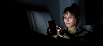 Mulher usa celular à noite no escuro deitada no sofá.