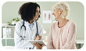 Médica sorridente conversando com paciente idosa em consultório.