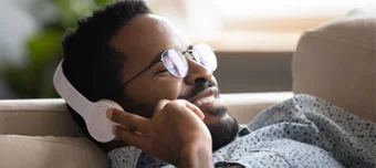 Homem sorrindo feliz, deitado no sofá, ouvindo música em seu fone de ouvido