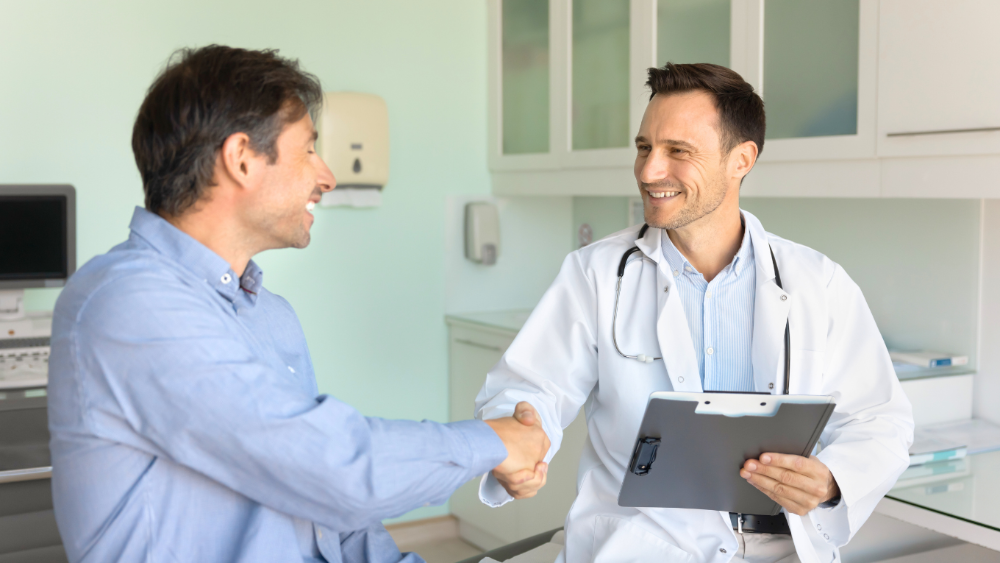 Médico em consultório cumprimenta paciente durante atendimento em unidade de oncologia, simbolizando cuidado humanizado e confiança.
