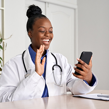 Médica sorrindo e acenando durante uma teleconsulta pelo celular.