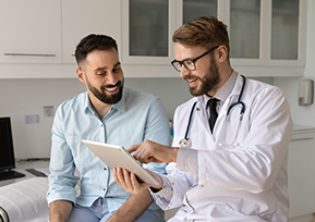 Médico mostra tablet a paciente sorridente em consultório.