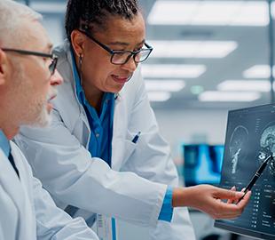 Dois médicos de jaleco branco, um homem e uma mulher, analisando exames de imagem do cérebro em uma tela de computador, simbolizando o trabalho do Centro de Medicina Diagnóstica (CMD).