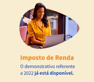 Mulher sorridente trabalhando em um notebook, com o texto Imposto de Renda - O demonstrativo referente a 2022 já está disponível sobreposto em um fundo laranja, simbolizando a disponibilidade de documentos para a declaração.