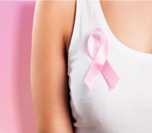 Peito de uma mulher com uma fita rosa de conscientização, simbolizando o Outubro Rosa e a importância do exame de toque e diagnóstico precoce do câncer de mama.