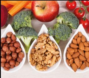 Alimentos saudáveis (brócolis, cenouras, maçã, tomates, avelãs, nozes e amêndoas) dispostos em tigelas e sobre uma superfície, simbolizando a importância da alimentação para a imunidade e prevenção de doenças infecciosas.