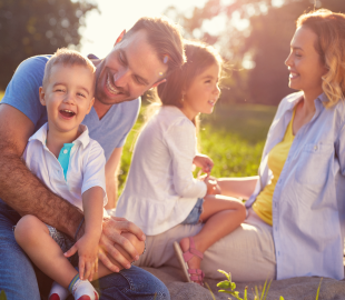 Família feliz com dois pais e duas crianças pequenas em um ambiente externo, sorrindo e interagindo, simbolizando a Atenção Primária à Saúde em Florianópolis.