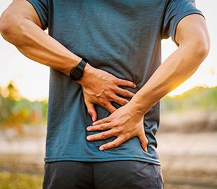 Homem de costas com as mãos na região lombar, expressando dor nas costas, ilustrando o tema de dor lombar.