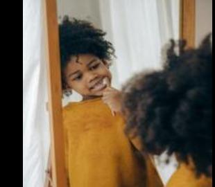Criança escovando os dentes em frente ao espelho, simbolizando a higiene bucal e a prevenção da halitose.