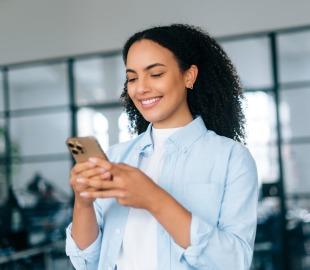 Mulher sorridente, vestindo camisa azul clara, usando o celular para dar feedback ou avaliar um serviço de saúde, simbolizando a importância da opinião do cliente.