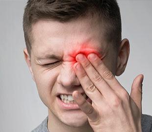 Homem com expressão de dor ou desconforto, segurando o olho com uma área vermelha destacada sobre ele, simbolizando irritação ou inflamação ocular como a conjuntivite.