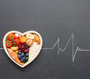 Alimentos saudáveis (tomates, nozes, aveia, salmão, mirtilos) dispostos em um recipiente em formato de coração, com um desenho de eletrocardiograma em um fundo escuro, simbolizando a saúde cardíaca e os riscos do colesterol alto.