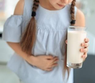 Criança com dor abdominal segura copo de leite, representando sinais de alerta para alergia alimentar infantil, como intolerância à lactose ou proteína do leite.