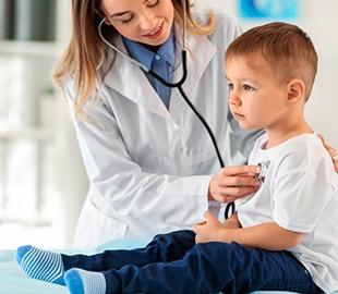 Cardiologista infantil feminina examinando o coração de um menino pequeno com um estetoscópio, ilustrando uma consulta de cardiologia pediátrica.