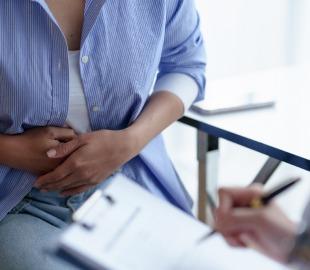 Mulher com as mãos no abdômen durante consulta ginecológica, representando investigação médica de cólicas menstruais intensas e possíveis causas