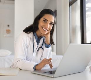 Médica sorridente em consultório realiza atendimento online por teleconsulta, representando especialidades médicas com consultas virtuais