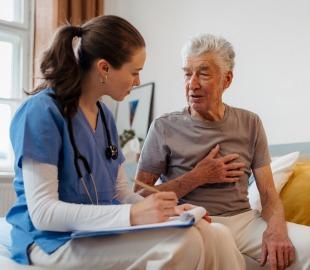 Enfermeira ou médica conversando com um paciente idoso que segura o peito, simbolizando a importância do cuidado e acompanhamento da saúde cardíaca.