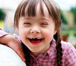 Criança com Síndrome de Down sorrindo e com os olhos fechados, expressando alegria, simbolizando a conscientização e compreensão da síndrome.