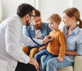 Médico realiza exame preventivo em criança durante consulta com a família, destacando os benefícios do plano de saúde na promoção da qualidade de vida