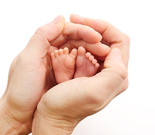 Mãos de um adulto segurando gentilmente os pequenos pés de um bebê recém-nascido, simbolizando o Dia Mundial da Prematuridade e os cuidados com bebês prematuros.