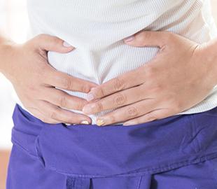 Mulher com as mãos sobre o abdômen, expressando desconforto ou dor na região da barriga, simbolizando os sintomas da Doença de Crohn.