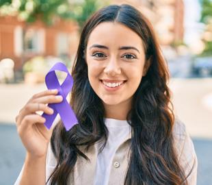 Mulher jovem sorridente segurando uma fita de conscientização roxa, simbolizando a conscientização sobre o Lúpus Eritematoso Sistêmico.