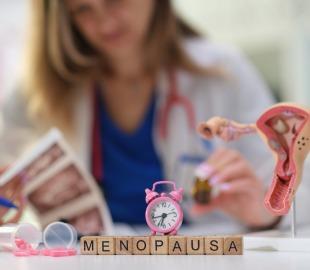 Médica ginecologista segura frasco de medicamento ao lado de maquete do útero e relógio rosa, simbolizando os cuidados na nova fase da vida da mulher