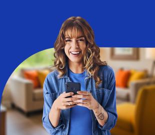 Mulher sorridente segurando um smartphone, com fundo azul e uma sala de estar desfocada, simbolizando a atualização de cadastro e o uso de tecnologia.