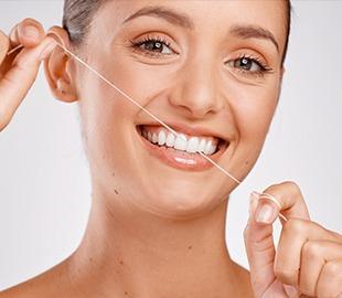 Mulher sorridente demonstrando o uso do fio dental para a higiene bucal, ilustrando dicas essenciais sobre odontologia.