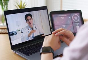 Pessoa se consultando um médico virtualmente em um computador, enquanto um tablet exibe dados de rastreamento do sono e saúde, simbolizando telemedicina e monitoramento da saúde.