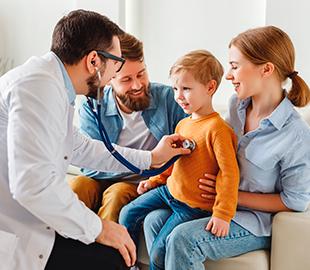 Médico examinando o coração de um menino pequeno com um estetoscópio, enquanto os pais sorriem ao lado, simbolizando os benefícios de um plano de saúde familiar.