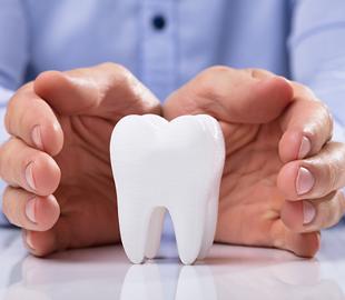 Mãos em formato protetor sobre um modelo de dente branco, simbolizando cuidado e tratamentos odontológicos estéticos.