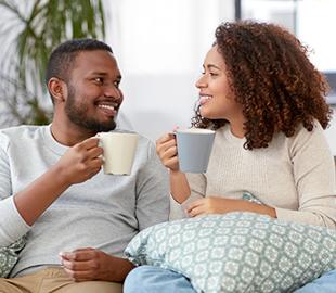 Casal sorridente e relaxado, cada um segurando uma caneca de chá, olhando um para o outro, simbolizando o bem-estar e o uso de plantas medicinais em chás.