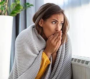 Mulher embrulhada em um cobertor, com as mãos no rosto, parecendo sentir frio e desconforto, simbolizando os sintomas da pneumonia.