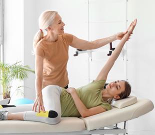 Quiropraxista auxiliando uma paciente deitada em uma maca a realizar um exercício de braço, ilustrando uma sessão de quiropraxia ou fisioterapia.