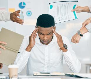 Homem com as mãos na cabeça, visivelmente estressado, cercado por múltiplas mãos oferecendo documentos e tarefas, simbolizando a síndrome de burnout e a sobrecarga de trabalho.