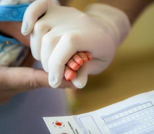 Profissional da saúde coleta sangue do calcanhar de um recém-nascido para o Teste do Pezinho, destacando a importância da triagem ampliada nos planos de saúde.