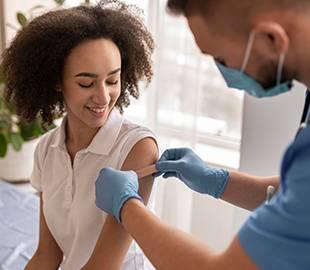 Mulher sorridente recebendo uma vacina no braço de um profissional de saúde, simbolizando a vacinação contra a gripe.