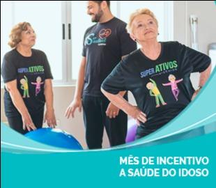 Duas idosas sorridentes em camisetas Super Ativos com um instrutor masculino ao fundo, praticando atividades físicas em um estúdio, simbolizando o envelhecimento ativo e a saúde do idoso.