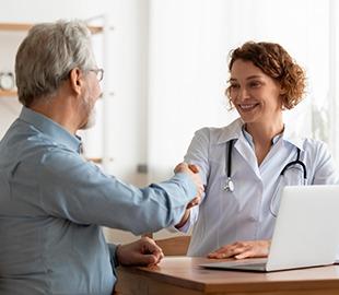 Médica sorridente de jaleco branco apertando a mão de um paciente idoso em um consultório, simbolizando a comunicação sobre a mudança de atendimento do Notrelabs Senador.