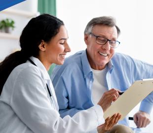 Médica sorridente de jaleco branco mostrando uma prancheta para um paciente idoso, simbolizando a comunicação sobre as mudanças de atendimento nas unidades Centro Clínico Pinhais e Centro Clínico Centro.