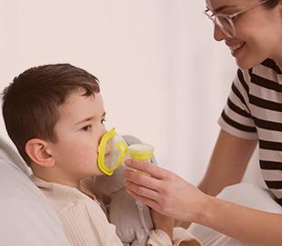 Mãe ou cuidadora auxiliando uma criança a usar uma máscara inaladora, simbolizando os cuidados com a saúde respiratória e a atenção às queimadas.