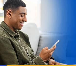 Homem jovem negro, sorridente, olhando para seu smartphone, simbolizando a Central de Serviços Online e Prático da Hapvida Clinipam.