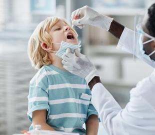 Profissional de saúde, usando máscara e luvas, aplicando vacina em gostas em uma criança pequena, simbolizando a vacinação e a prevenção da poliomielite.