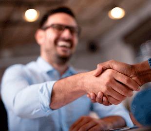 Homem sorridente em segundo plano apertando a mão de outra pessoa em primeiro plano, simbolizando a contratação ou acordo de um convênio médico individual.
