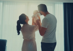 Família sorrindo enquanto segura um bebê ao nascer do sol, representando o cuidado e a transformação da Hapvida.